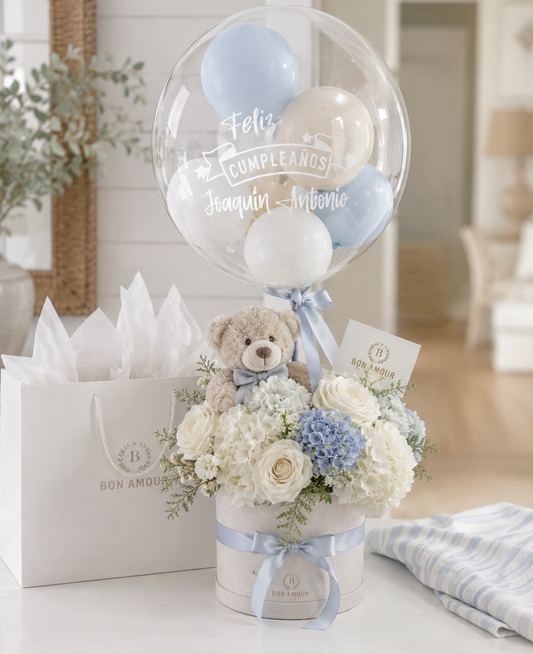 Bouquet of flowers with a teddy bear and balloons in a bubble, placed on a table.