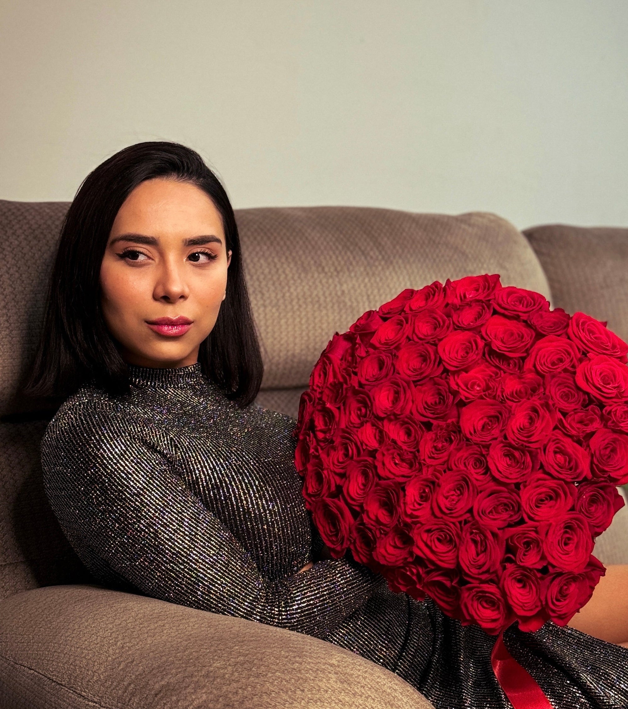 Woman holding a large bouquet of red roses on a couch